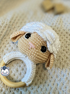 Crochet sheep baby rattle with white and beige amigurumi head on a natural wooden ring.