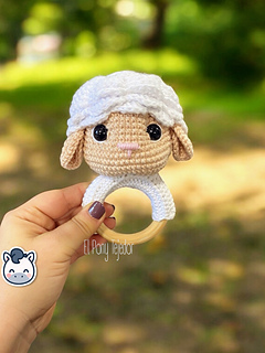 Crochet sheep baby rattle with white and beige amigurumi head on a natural wooden ring.