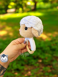 Crochet sheep baby rattle with white and beige amigurumi head on a natural wooden ring.