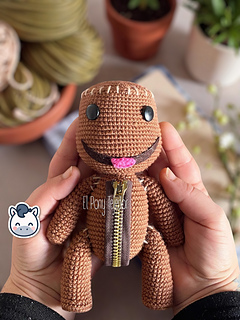 Sackboy Amigurumi crochet pattern in brown yarn featuring a chest zipper detail and black button eyes.