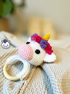 Crochet amigurumi pattern of a baby unicorn rattle with a golden horn, pink and purple mane on a wooden ring.