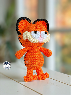 Crochet orange cat amigurumi inspired by Garfield, featuring rounded cheeks, embroidered details and black stripes on the back.