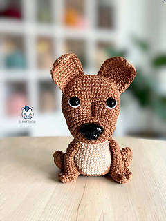 Crochet Amigurumi pattern of a brown and beige American Staffordshire dog sitting on a white wooden surface, perfect for an instant download pattern.