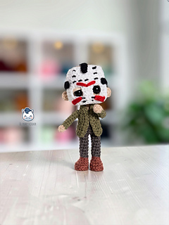 Handmade Jason Voorhees amigurumi inspired by Friday the 13th, featuring his iconic white hockey mask with red markings, green jacket, and dark pants. A horror-themed crochet doll made with a step-by-step PDF pattern, perfect for Halloween and slasher movie fans.