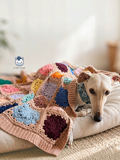 Light-coloured greyhound resting on a sofa under the Granny Flowers crochet blanket, with colourful floral squares and beige edging.