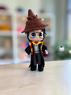 Two Harry Potter amigurumi dolls shown from the front on a wooden table. On the left, Harry wears a red and gold Quidditch uniform and holds a brown broom. On the right, he wears a black cloak, a red and gold scarf and a brown Sorting Hat. Both have black hair and round glasses. The El Pony Tejedor logo appears on the left.