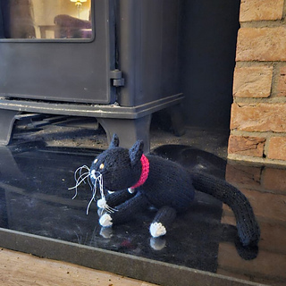 Black and white knitted cat beside the log burner