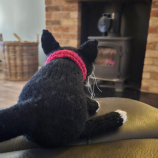 Black and white knitted cat in front of the fire