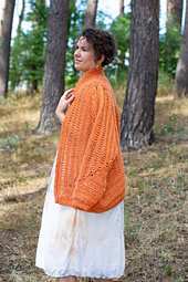 Woman draped in a warm, pumpkin-colored crochet cardigan, highlighting its cozy texture and stylish design.