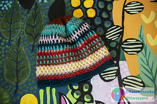 Colorful crochet beanie with stripes, laid on a bright painted background.