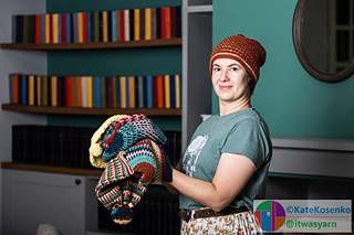 Wearing one herself, a woman displays a collection of colorful crochet hats in various sizes.