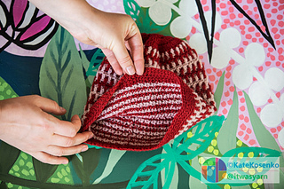 Hands holding a red and pale pink striped crochet beanie.