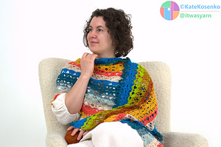 Woman adjusting crochet shawl near face while sitting in chair, showcasing drape and texture