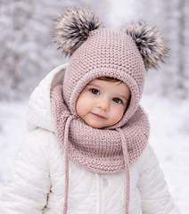 Knitted toddler balaclava hat with bear ears and drawstring, worn by a baby sitting among autumn leaves. The hooded hat covers the head, ears, neck, and chest, keeping the child warm.