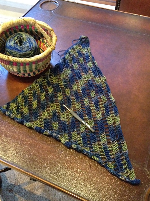 An in-progress crochet project in blue and green with diagonal rows of 