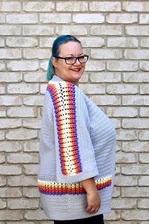 Side profile of curvy female with blue hair wearing a grey cardigan with accent purple, pink, orange, yellow and white puff stitches.