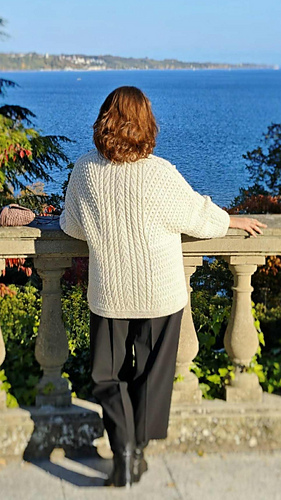 
Discover the artistry of the back panel design. A commanding vertical cable runs along the spine, strategically lengthening the oversized silhouette while maintaining a refined, structured appearance. The dynamic diagonal cable stitches across the shoulders create visual flow and movement, while the Herringbone stitch at the hem anchors the design with timeless elegance. This thoughtful three-part composition — vertical extension, diagonal movement and horizontal grounding demonstrate expert pattern placement that flatters every body shape. 
