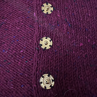I used large, brass prym snaps. I tacked through the stabilizing ribbon one time through each little aperture in the snaps then stitched just to the knit, which gave me a very smooth line
on the outside.