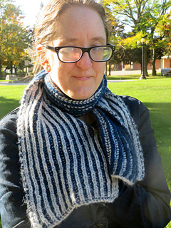 Image Description: A woman wearing a bulky-knit reversible scarf. The scarf is knit in two-colour fisherman's ribbing, forming vertical stripes in two colours, off white and dark blue.