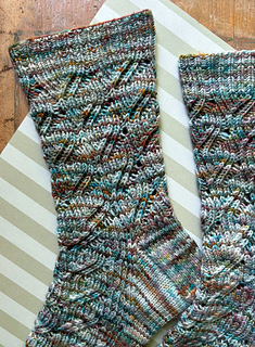 Image Description: a pair of ribbed lace socks laying flat. They are knit in a multicoloured variegated yarn and have a diagonal lace motif on the leg and the top of the foot
