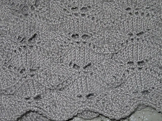 [Image Description: a close up of a scalloped knit lace pattern done in silver-grey yarn.]