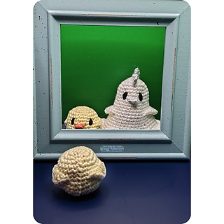 A small crochet chick standing with its back to the camera and in front of a mirror. In the mirror we can see the chick's front, and next to it a tall ghostly chicken, also crocheted.