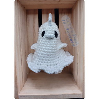 A small crochet ghost chicken floating inside a wooden box.