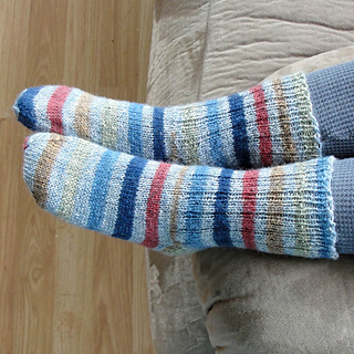 Small boy's feet wearing striped ribbed knit socks while sitting on a couch.