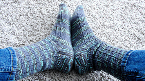 Striped purple-and-turquoise Just Plain Socks. Cuff-down ribbed socks with eye-of-partridge heel being worn by a woman with the soles of her feet pressed together.