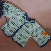 Mint green hexie cardigan with dark blue border, photographed on a wooden background.