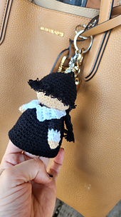 Crochet Wednesday Addams keychain pattern listing photo showing the finished mini doll hanging from a beige bag