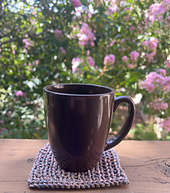 Sample of coaster in recommended yarn with a mug sitting on top of it. Stockinette section is hidden by mug.