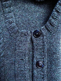 Showing detail of underarms of blue vest including buttons and buttonholes, armhole ribbing and knit-on trim.