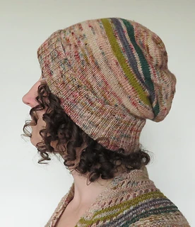 Brunette woman with curly hair wearing a pink, slouchy knit hat with a few stripes - white background.