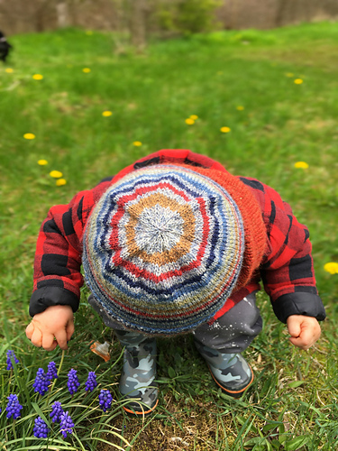 Toddler boy looking at the grass and wearing a striped knit hat showing the circles on the crown.