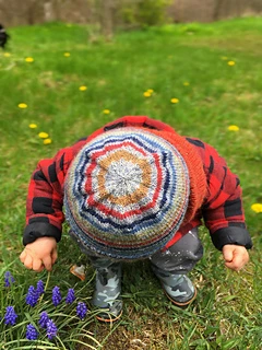 Toddler boy looking at the grass and wearing a striped knit hat showing the circles on the crown.