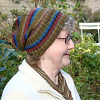 An older woman with short hair, glasses and a white jacket wearing a green striped slouch hat with a wide ribbed brim folded up.