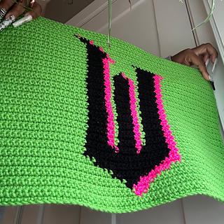 Finished tapestry features green, black, and pink yarn that form a W letter