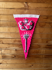 Pink and white crochet pennant hangs on a wooden wall