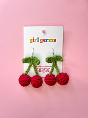 crochet earrings are shown against a pink backdrop. They are shown in packaging that reads "girl germs."