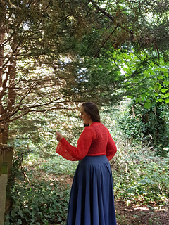 Smiling woman in coral crochet lace wrap cardigan  stands in a forest facing away