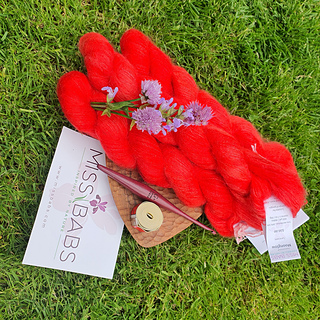 fluffy coral yarn and wooden crochet hook on a small wooden stand on a lawn