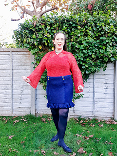 Smiling woman in coral crochet lace wrap cardigan wrapped closely stands in a garden spreading her arms wide