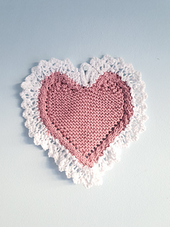 Heart-shaped knitted cloth with white lace edges hung on a nail on a blue wall