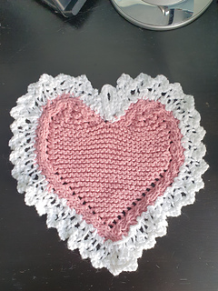 Heart-shaped knitted cloth with white lace edges on a wooden table 