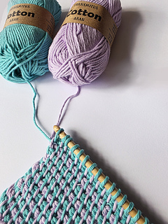In-progress photo of Tunisian crocheted square cloth worked in a turquoise and lavender pattern on a wooden hook with yarn in the background.