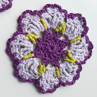 crocheted dark and light purple flower coaster with green detail