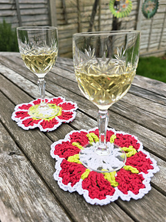 crocheted red and white flower coasters with green detail with stem glasses holding a light yellow drink on a wooden table (coaster B is at front)