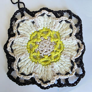 crocheted cream and beige flower square with green detail and black edging