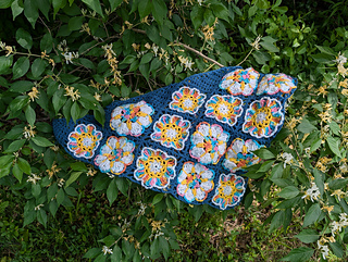 Blue lace triangular shawl with bright floral granny squares laid flat